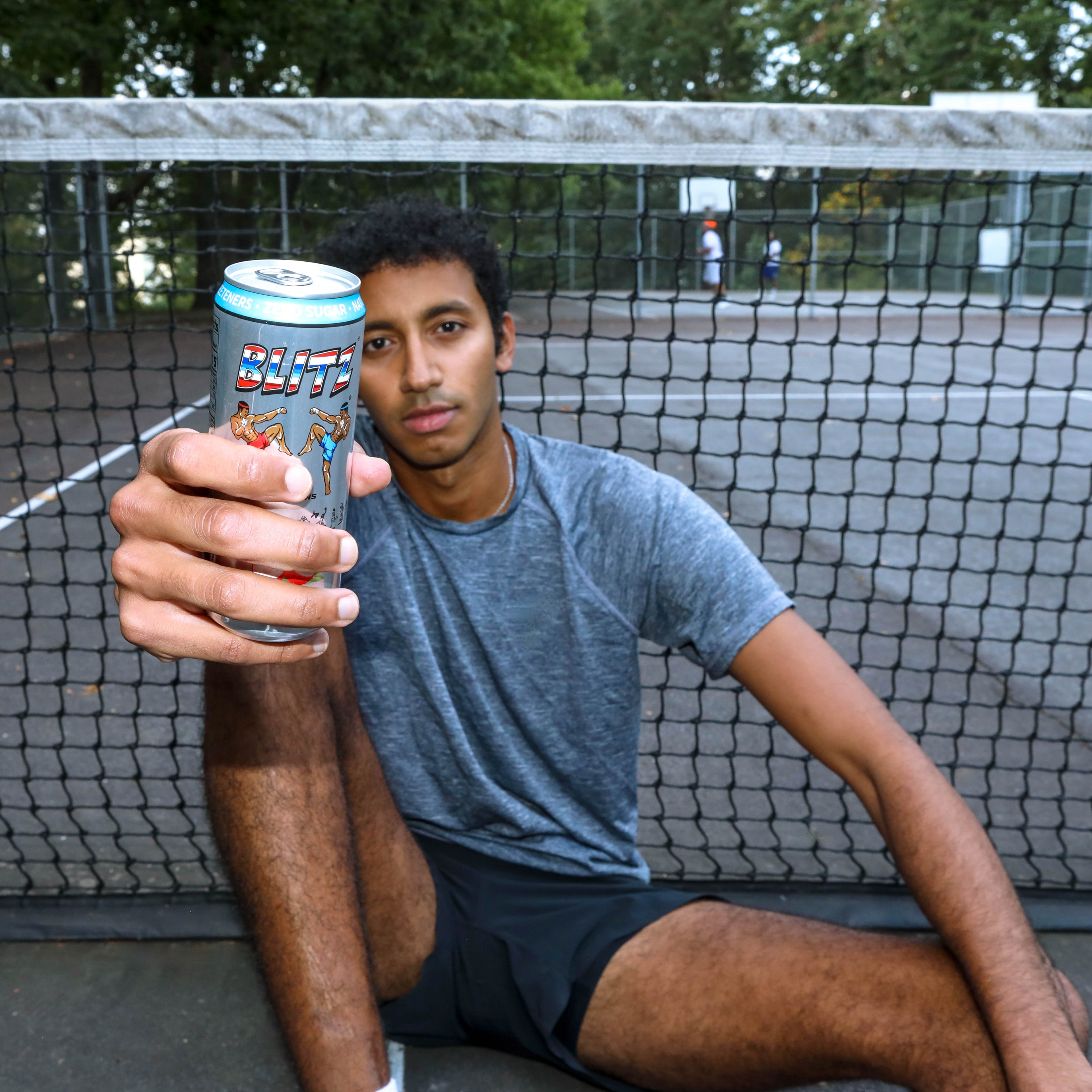 Person holding a can of BLITZ energy drink on a tennis court